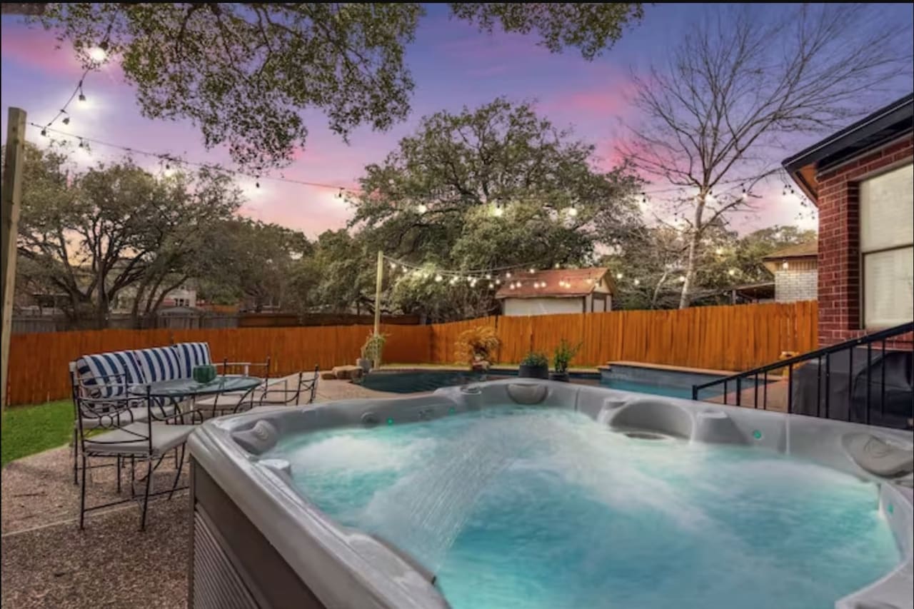 Shady Oak Retreat bubbling hot tub at dusk with string lights overhead and the pool beyond